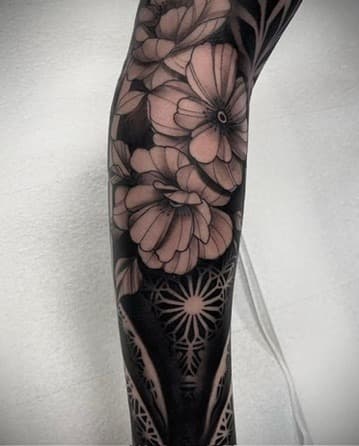 Blackwork floral leg piece — bold geometric flowers with solid black negative space wrapping the calf